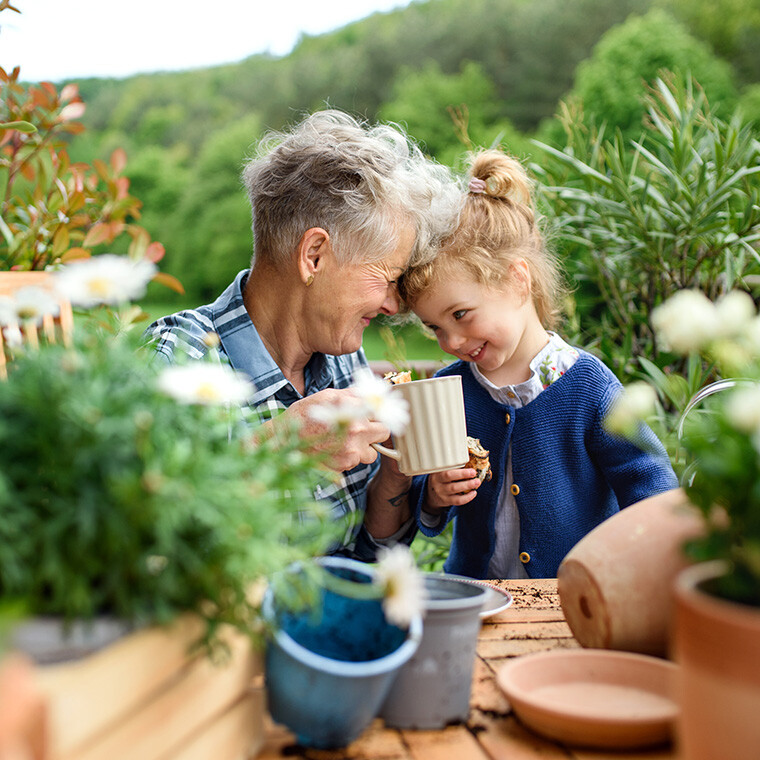 Senior grandmother with small granddaughter gardening on balcony in summer